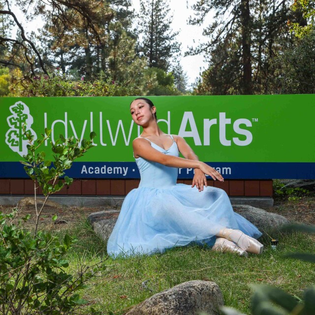 A dancer poses in front of the Idyllwild Arts sign.