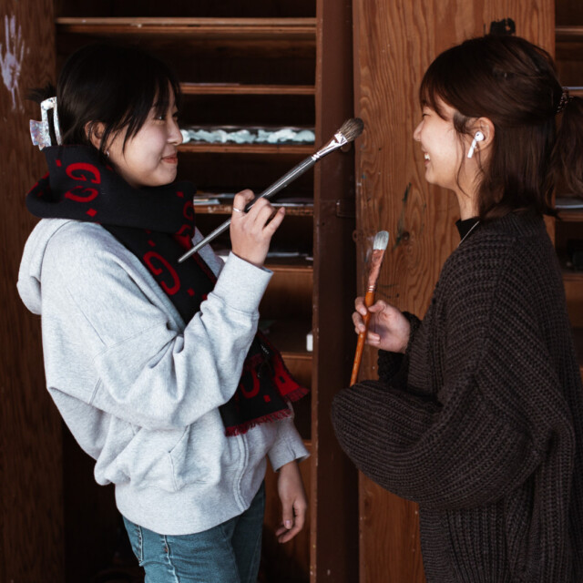 Two students holding paint brushes.